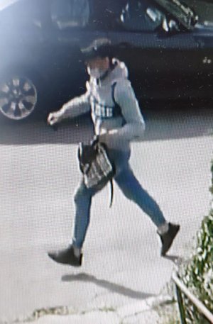 Na zdjęciu widać jak mężczyzna ubrany w siwą sportową bluzę z ciemnym napisem z przodu, niebieskie jeansy ściągane gumką przy kostkach, białe skarpetki, ciemne buty i ciemną czapkę z daszkiem typu bejsbolówka, biegnie z torebką, którą siła wyrwał kobiecie.