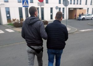 Na zdjęciu widać policjanta umundurowanego po cywilem, który prowadzi zatrzymanego 36-latka ubranego w granatowa kurtkę i jeansy.