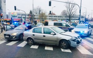 Na zdjęciu widać srebrnego opla astrę z uszkodzonym przodem w wyniku celowego wjechania w policyjny radiowóz. Tym samochodem uciekali dwaj zatrzymani obywatele Gruzji i tym samym pojazdem chcieli potracić policjantkę. Samochód stoi na skrzyżowaniu, w miejscu zatrzymania podejrzanych. Obok niego stoją nieoznakowane pojazdy policyjne hyundai i opel. Na dachu mają włączone niebieskie światła.