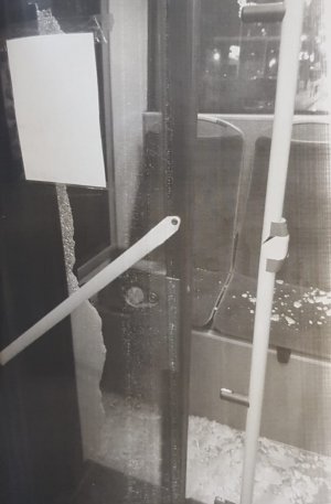 Zdjęcie przedstawią zdjęcia wybitej bocznej szyby w autobusie. Widać na nich fragmenty szkła w ramie okiennej oraz rozrzucone w pobliżu drobne kawałki.