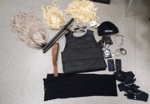 Zdjęcie przedstawia przedmioty zabezpieczone przez policjantów, które były wykorzystywane przez podejrzanego do popełniania przestępstwa. Na zdjęciu widać trzy damskie peruki, kamizelkę kuloodporną, palkę teleskopową i palkę typu tonfa, latarki taktyczne, kajdanki, czarne rękawiczki, czarną czapkę z napisem ochrona, imitację odznaki policyjnej, brązowy szeroki pasek.