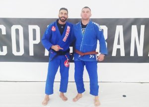 Zdjęcie przedstawia zawodników brazylijskiego jiu-jitsu. Po lewej stronie stoi wielokrotny Mistrz Świata Braulio Estima, który wcześniej wręczył brązowy pas w BJJ  stojącemu prawej stronie mł. asp.Sebastianowi Garbienia.