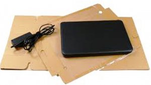 Zdjęcie przedstawia laptop wraz z ładowarką położony na tekturowym opakowaniu.