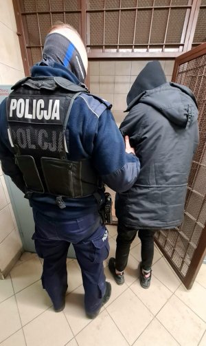 Zdjęcie przedstawia umundurowanego policjanta z zatrzymanym 18-latkiem. Mężczyźni odwróceni są tyłem do obiektywu.