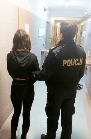 Zdjęcie przedstawia umundurowaną policjantkę z zatrzymaną 18-latką. Kobieta ma kajdanki założone na ręce z przodu.