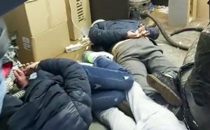 Na zdjęciu trzej zatrzymani mężczyźni leżący w garaży na podłodze. Odwróceni są twarzami do podłoża. Mają założone kajdanki na rękach z tyłu.