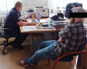 Zdjęcie przedstawia Policjanta dzielnicowego wykonującego czynności z zatrzymanym mężczyzną.
