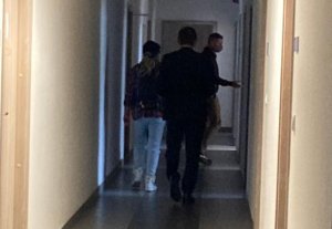 Po lewej stronie kobieta podejrzana o kierowanie pojazdem w stanie nietrzeźwości. Po prawej stronie nieumundurowany policjant prowadzący kobietę na przesłuchanie.