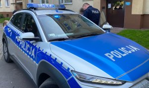Policjant umundurowany rozmawiający z uczestnikami pikniku stoi obok radiowozu policyjnego.
