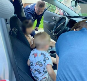 Policjant umundurowany rozmawiający z uczestnikami pikniku pokazuje dzieciom  radiowóz policyjny.