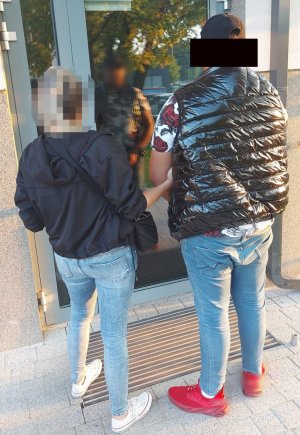 Policjanta trzyma mężczyznę za zgięcie w łokciu.