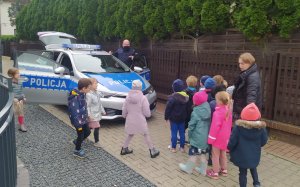 Na zdjęciu dzielnicowy prowadzi zajęcia z dziećmi z Przedszkola Frajda na warszawskim Wilanowie  mówiąc o tym, jak postępować, aby dni mijały bezpiecznie w domu, w przedszkolu, w świecie wirtualnym i na drodze.