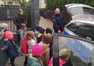 Na zdjęciu dzielnicowy prowadzi zajęcia z dziećmi z Przedszkola Frajda na warszawskim Wilanowie  mówiąc o tym, jak postępować, aby dni mijały bezpiecznie w domu, w przedszkolu, w świecie wirtualnym i na drodze.