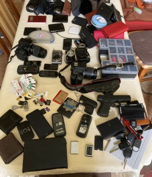 Na zdjęciu na blacie biurka zabezpieczone przez policjantów przedmioty pochodzące z kradzieży kieszonkowych w postaci etui, telefonów komórkowych, aparatów fotograficznych, pen drive, atrapa pistoletów.