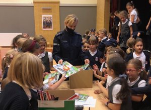 Policjantka rozdaje dzieciom materiały edukacyjne w ramach spotkania dotyczącego bezpieczeństwa.