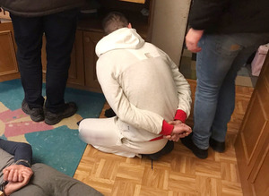 Na podłodze w mieszkaniu leżą i siedzą osoby zatrzymane. Mają kajdanki założone na ręce z tyłu