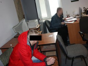 Nieumundurowany policjant wykonuje czynności z zatrzymanym mężczyzną.