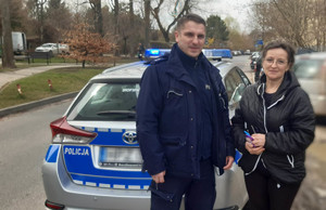 Z lewej strony na tle radiowozu stoi umundurowany policjant. Obok niego kobieta narodowości ukraińskiej której pomógł w odnalezieniu wnuka.