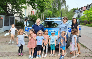 Policjanci prowadzą zajęcia z dziećmi, opowiadając o zawodzie policjanta i bezpieczeństwie. Na zdjęciach dzieci oglądają z bliska i od wewnątrz policyjny radiowóz i wyposażenie służbowe.