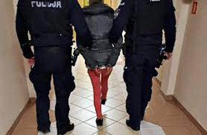 Zatrzymana kobieta prowadzona przez dwóch umundurowanych policjantów.
