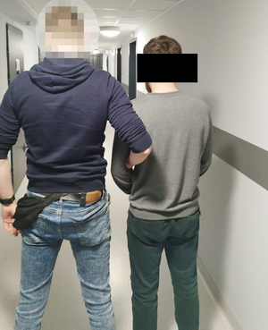 Nieumundurowany policjant prowadzi zatrzymanego mężczyznę.