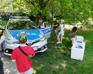 Policjanci prezentują radiowóz policyjny zgromadzonym wokół dzieciom.