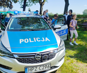 Policjanci prezentują radiowóz policyjny zgromadzonym wokół dzieciom.