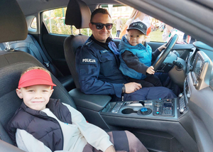 Umundurowany policjant siedzi w radiowozie z dziećmi.