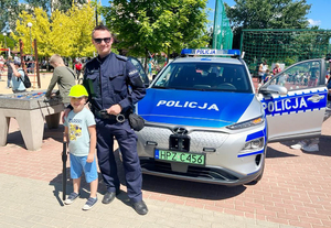 Umundurowany policjant stoi przy radiowozie, a obok dziecko.