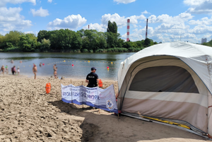 Policjant stoi na plaży i obserwuje teren kąpieliska.