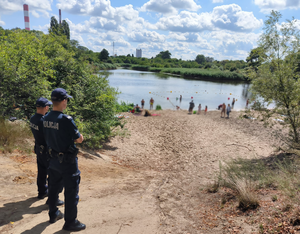 Dwóch policjantów stoi i obserwuje teren plaży przy kąpielisko wodnym.