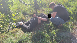 Na zdjęciu widać mężczyznę leżącego na trawie. Mężczyzna ma założone kajdanki na ręce trzymane z tyłu. Obok niego w pozycji nachylonej widać funkcjonariusza ubranego po cywilnemu.
